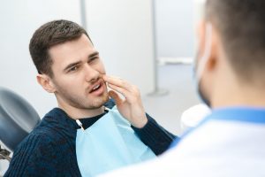 A man sitting in the dental treatment chair holding his cheek in pain